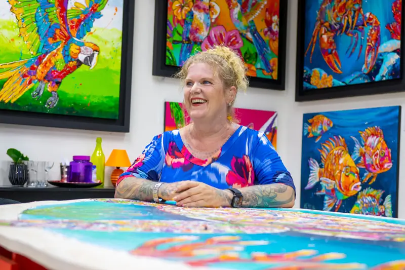 Renata smiling in her gallery surrounded by colorful paintings